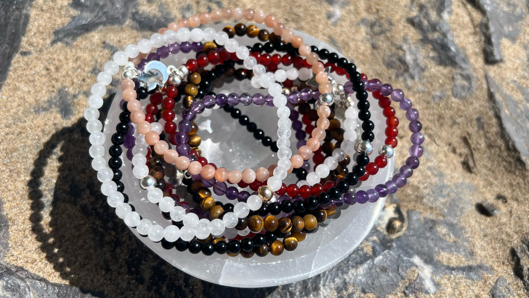 Crystal bracelets in a selenite bowl on a sandy rock