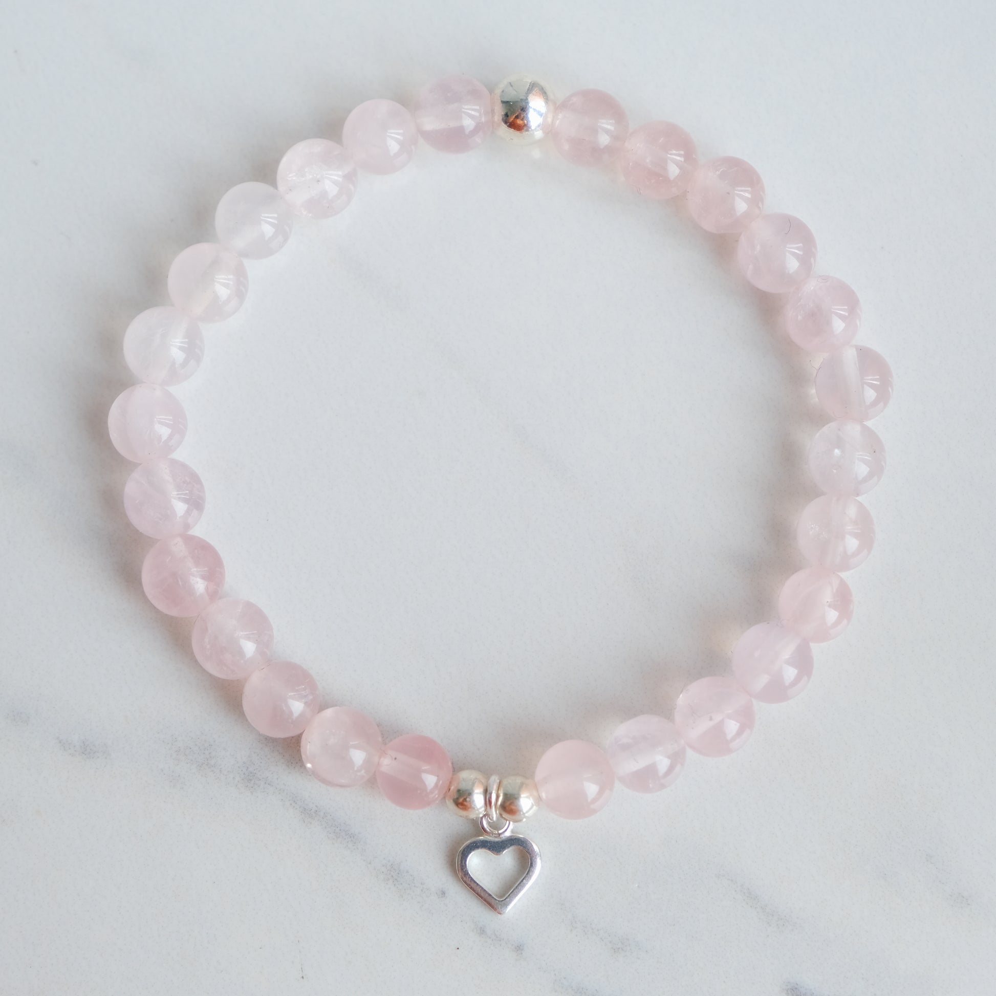 A rose quartz crystal bracelet with silver love heart charm from above