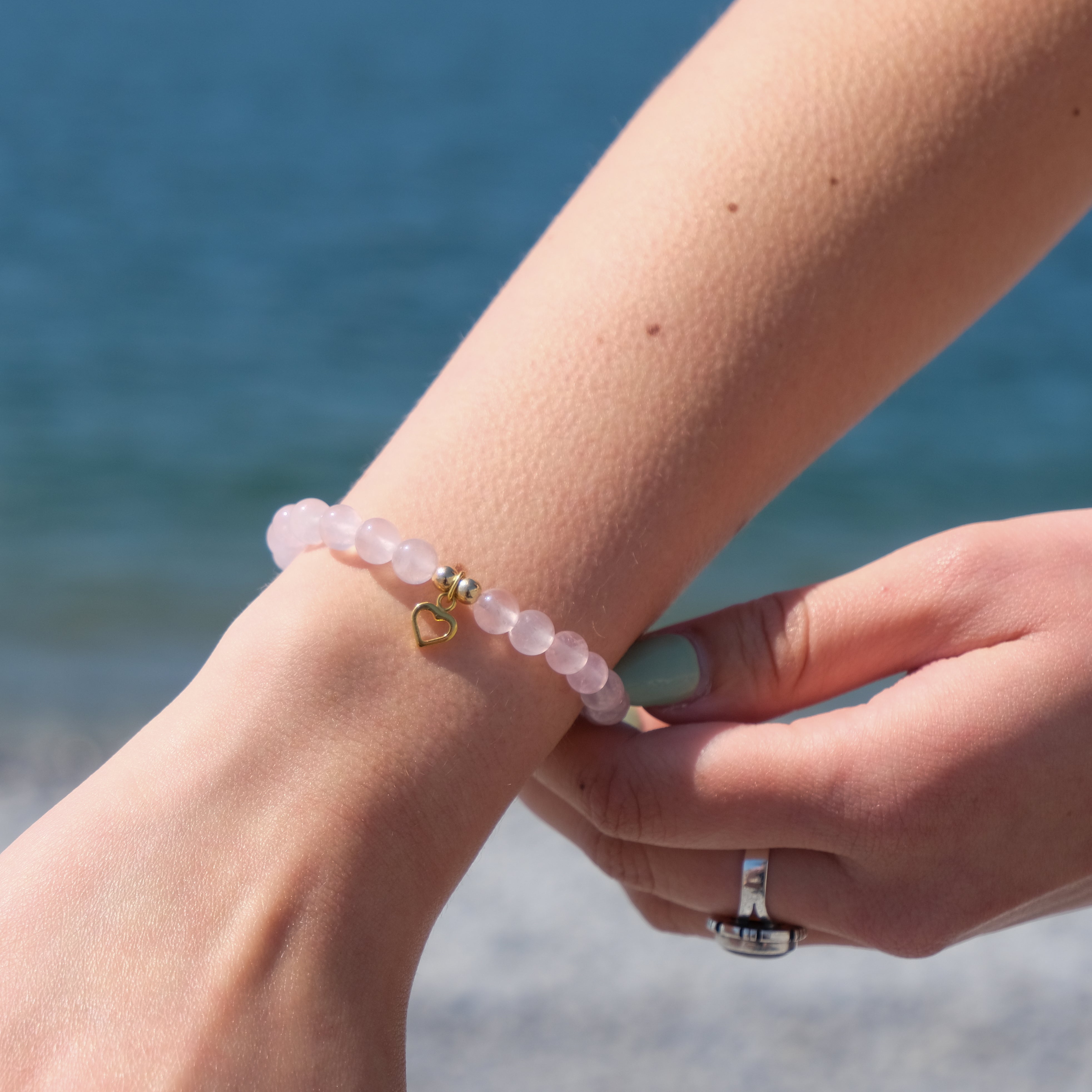 A model wearing a rose quartz crystal bracelet with gold love heart charm