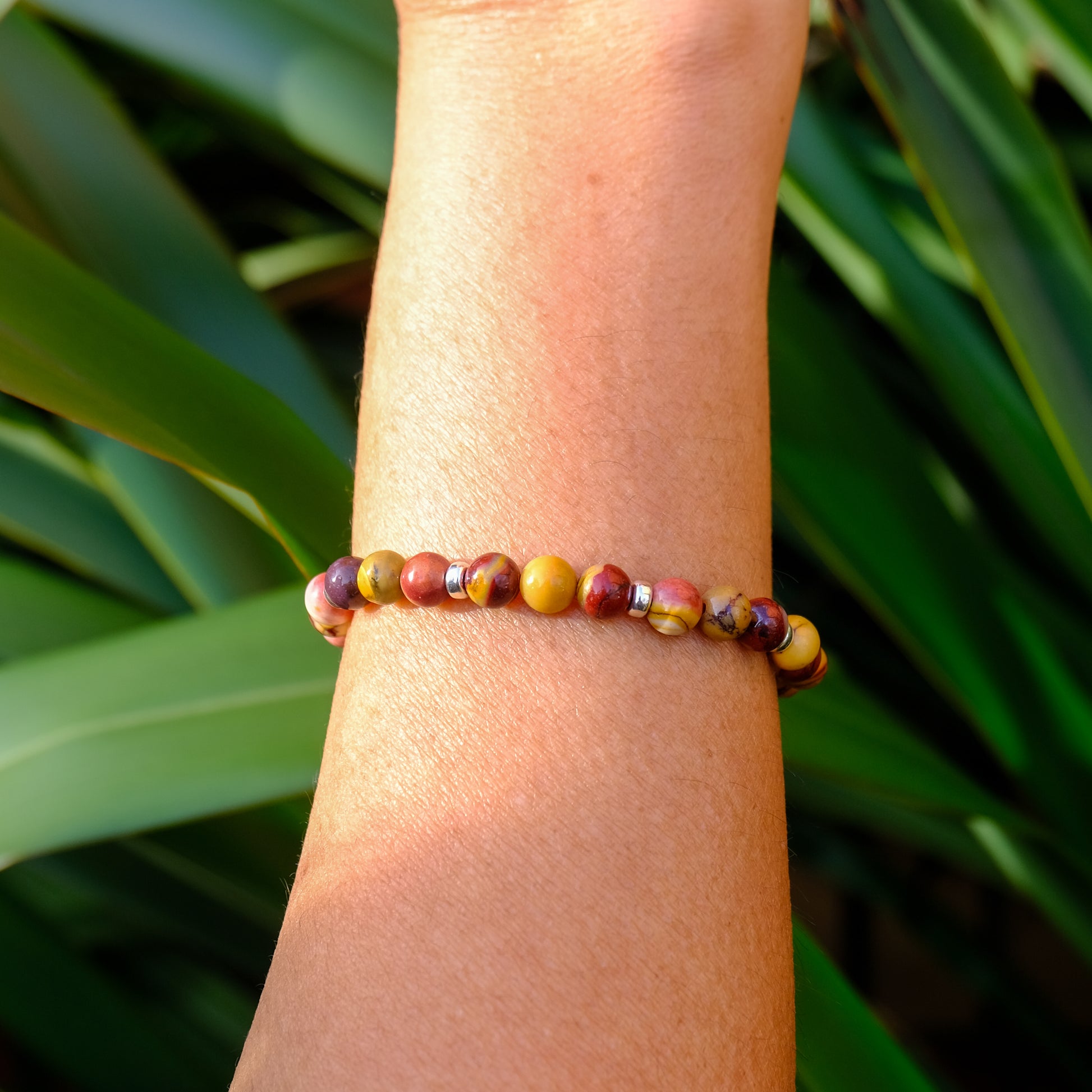 A 6mm mookaite gemstone bracelet with gold accessories worn on a model's wrist