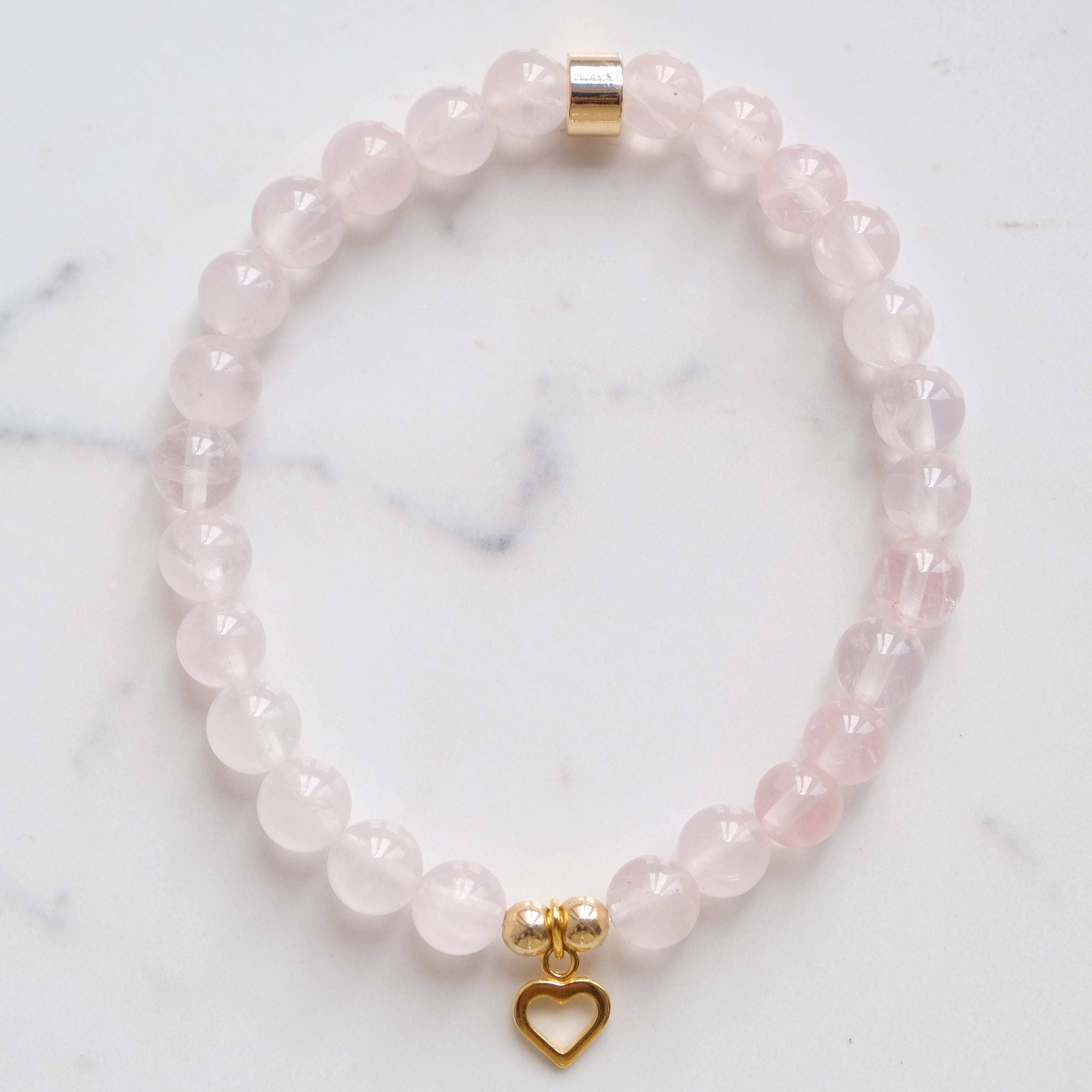 A rose quartz crystal bracelet with gold love heart charm from above